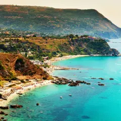 Vista mozzafiato del capo Vaticano a Tropea, con il mare cristallino che lambisce le spiagge affollate e le scogliere verdi.