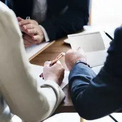 Ludzie przy stole podpisują dokumenty, jeden z nich trzyma długopis.