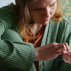 Kobieta w zielonym swetrze przegląda dokumenty na telefonie, być może wniosek o zasiłek chorobowy.