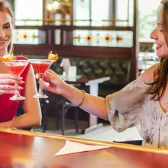 Dwie przyjaciółki wznoszą toasty drinkami przy barze. Idealny weekend z przyjaciółką!