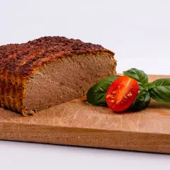 Pokrojony pasztet na desce z pomidorkiem koktajlowym i bazylią.
