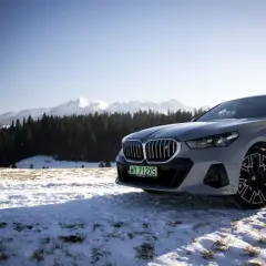 Szare BMW i5 na tle ośnieżonych gór i lasu.