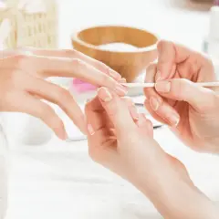 Dłoń przygotowywana do manicure hybrydowego. Delikatne ruchy patyczkiem usuwają skórki, by uniknąć uczulenia na hybrydę.