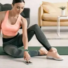 Frau in Sportkleidung sitzt auf einer Matte und bedient ihr Smartphone.