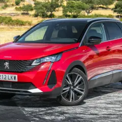 Opiniones del motor Peugeot 3008 1.5 HDI 130 CV: SUV rojo brillante aparcado en un camino rural con vegetación seca al fondo.