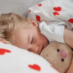 Śpiące dziecko przytula misia. Marzy o dniu pełnym słońca i zabawy, może nawet o nauce pływania w swojej pianka do pływania dla dziecka.