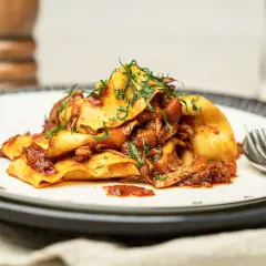 Herzhaftes Pasta Ragu mit breiten Nudeln, übergossen mit einer reichhaltigen Fleischsauce und garniert mit frischen Kräutern.