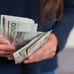 Dłonie trzymające plik banknotów 100 zł. To może być darowizna od rodziców na nowy cel.