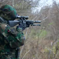 Żołnierz w kamuflażu celuje z karabinu snajperskiego. Widać lunetę, przez którą obserwuje cel, a zjawisko paralaksy w lunecie jest kluczowe dla precyzyjnego strzału.