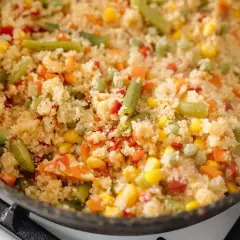 En varm och färgglad couscousrätt med gröna bönor, majs, morötter och paprika i en stekpanna.