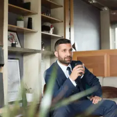 Elegancki mężczyzna w garniturze, z drinkiem w dłoni, emanuje spokojem i pewnością siebie w towarzystwie.