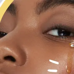 Nahaufnahme eines Gesichts, das Vitamin E Öl auf die Haut aufträgt. Ein Tropfen Öl fällt von einer Pipette auf die Wange.