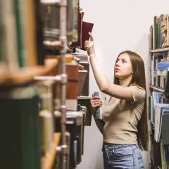 Młoda kobieta w bibliotece szuka inspiracji, zastanawiając się, jakie gatunki literackie są najbardziej poszukiwane przez wydawców w 2026.