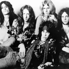 Aerosmith członkowie w rockowym stylu, z długimi włosami i charakterystycznymi strojami.