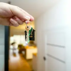 Klucze do nowego mieszkania od dewelopera. W tle widać wnętrze, drzwi i jasne światło.