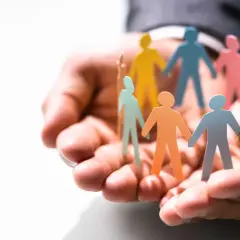 Hands cradle colorful paper people, symbolizing the benefits of equality, diversity, and inclusion in the workplace.