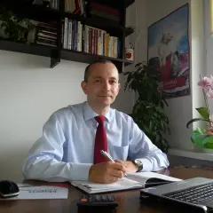 Mężczyzna w jasnej koszuli i czerwonym krawacie siedzi przy biurku, pisząc w notatniku.