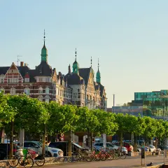 Kopenhaga ceny: zabytkowe budynki i nowoczesna architektura nad wodą, z rzędem drzew i zaparkowanymi samochodami.