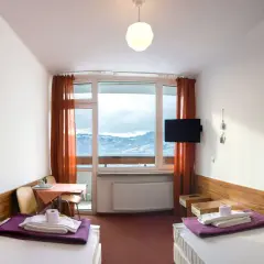 Pokój w dzwonkówka sanatorium uzdrowiskowe z widokiem na zimowe góry. Dwa łóżka, stolik, telewizor i balkon.