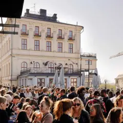 Folk trängs på Mosebacke terassen en solig dag. En stor folkmassa njuter av stämningen framför en gul byggnad.