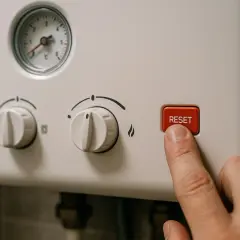 Palec naciska przycisk RESET na piecu gazowym dwufunkcyjnym, który sam się włącza.
