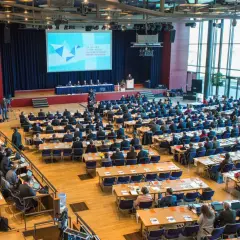 Große Versammlung mit vielen Zuhörern, die auf eine Bühne blicken. Die Bedeutung einer Synode wird hier durch die Präsentation und die Anwesenheit vieler Menschen verdeutlicht.