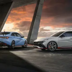 Dwa sportowe Hyundai sedan w kolorach niebieskim i jasnoszarym stoją pod betonowym mostem podczas zachodu słońca.