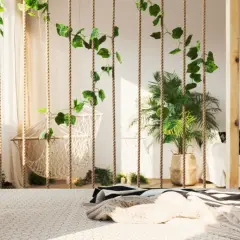 Grüne Ranken zieren Seile, die als Raumteiler Ideen zum Selbermachen dienen. Ein Hängesessel und Pflanzen schaffen Boho-Flair.