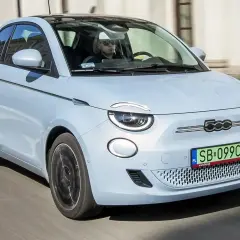 Jasnoniebieski fiat elektryczny 500 z czarnym dachem jedzie ulicą. Kierowca w okularach przeciwsłonecznych prowadzi auto.