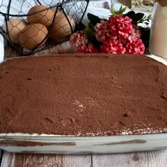 Tiramisù fatto in casa, una ricetta con panna che promette golosità. Uova fresche e cacao in polvere completano la scena.