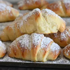 Brioches fatte in casa, dorate e soffici, cosparse di zucchero a velo. Un dolce profumo che invita a gustare la colazione.