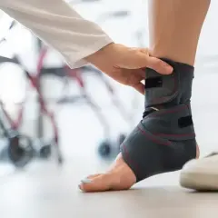 Rehabilitacja po urazie: specjalista zakłada stabilizator na staw skokowy, przygotowując pacjenta do badania rezonansem.