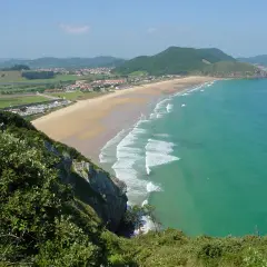 Vista panorámica de la playa de Berria, con arena dorada, aguas turquesas y colinas verdes al fondo.