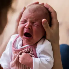 Ein Neugeborenes schreit laut, während es von Eltern gehalten wird. Die Frage, warum schreien Babys nach der Geburt, beschäftigt viele.