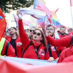 Frau mit Pfeife und weißem Tuch winkt, umgeben von roten Fahnen und Menschen bei einer Demonstration. Sie ist die Vorsitzende der IG Metall.