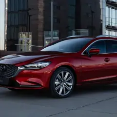 Czerwona Mazda 6 kombi na tle nowoczesnego budynku. Poznaj jej imponujące mazda 6 wymiary i styl.