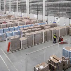 Duży magazyn z paletami towarów, pracownicy obsługują wózki widłowe. Widać wyraźnie strefę buforową, co to jest - to przestrzeń oddzielająca różne obszary.
