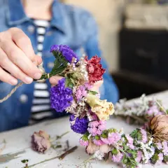 Hände binden bunte Trockenblumen zu einem Kranz. Ein schönes Projekt, um Trockenblumen selbst zu machen.
