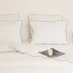 Parure de lit blanche avec passepoil vert, idéale pour un lit 140x190. Un magazine et des roses apportent une touche décorative.
