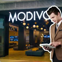 Elegancki mężczyzna w garniturze przegląda tablet przed sklepem MODIVO. W tle widać promocje CCC GPW.