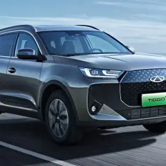 Szary SUV Chery Tiggo 7 z zielonym napisem TIGGO 7 na grillu, jadący po drodze.