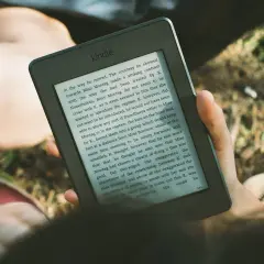 Une personne lit un livre sur une liseuse, profitant du soleil. L'encre numérique offre une lecture confortable en extérieur.