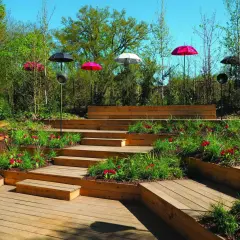 Escalier extérieur en bois avec des parterres de fleurs et des parasols colorés. La norme hauteur marche escalier extérieur est respectée pour un accès sûr.