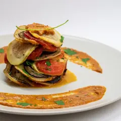 Ein gestapeltes Ratatouille-Rezept auf einem Teller, garniert mit Sauce und Kräutern.