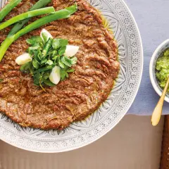 En tallrik med kibbeh nayyeh, rå köttfärs kryddad med bulgur och örter, toppad med vitlök, mynta och chili. Serveras med en grön sås.
