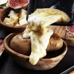 Fromage fondu coulant sur une pomme de terre, signe d'une raclette réussie. Accompagné de charcuterie et de figues.