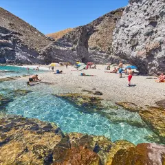 Descubre qué ver en Carboneras: una cala rocosa con aguas cristalinas y gente disfrutando del sol y el mar.