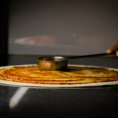 Rozsmarowywanie sosu pomidorowego na cieście pizzy. To kluczowy etap leżakowania ciasta na pizzę, przygotowujący je do dalszych etapów.