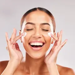 Mujer sonriente aplicándose crema en el rostro. Descubre para qué sirve la niacinamida en la piel y luce radiante.