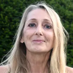 Portret Beaty Pawlikowskiej z blond włosami i niebieskimi oczami na tle zieleni.